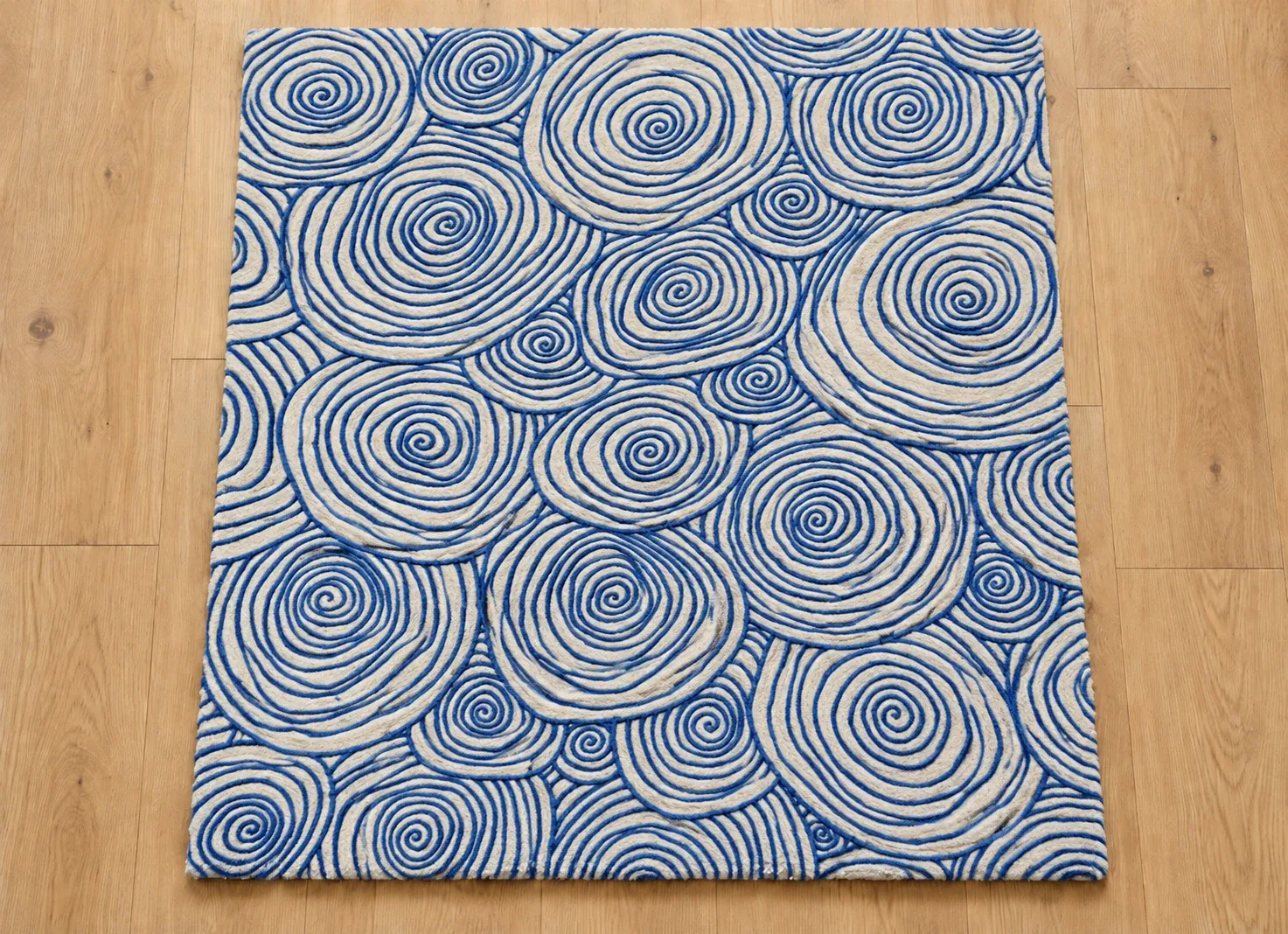 An empty rectangular tufted rug in hand-drawn cobalt blue line spirals on cream, on an oak floor, waiting for a pet